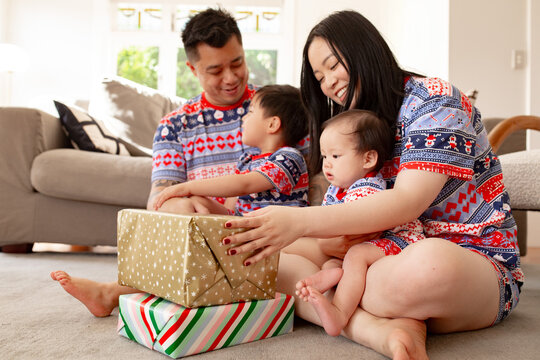Two Asian parents with their two young kids sitting on the floor with their presents