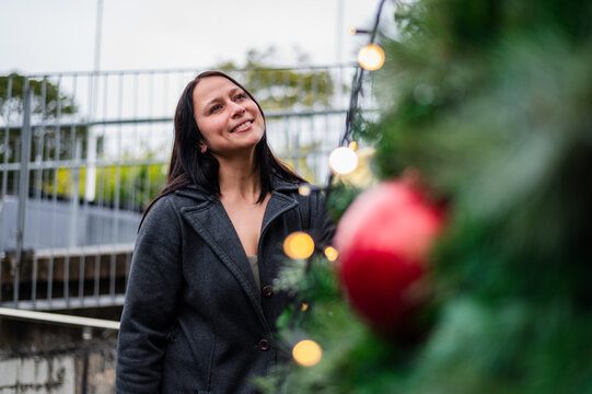 Woman standing near Christmas decorations, smiling as she looks up at the lights
