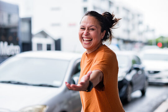 Woman standing on a city street reaching out and laughing while cars pass by on a busy day