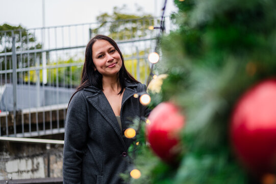 Woman smiling while standing by a Christmas tree with decorations in a public space