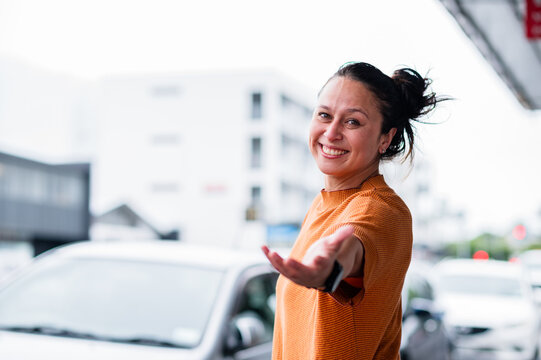 Woman standing in city street and smiles while reaching out her hand near the cars parked outside
