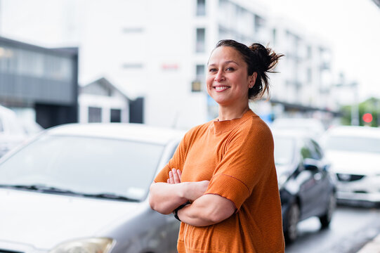 Person outdoors in orange with arms crossed near parked cars in New Zealand