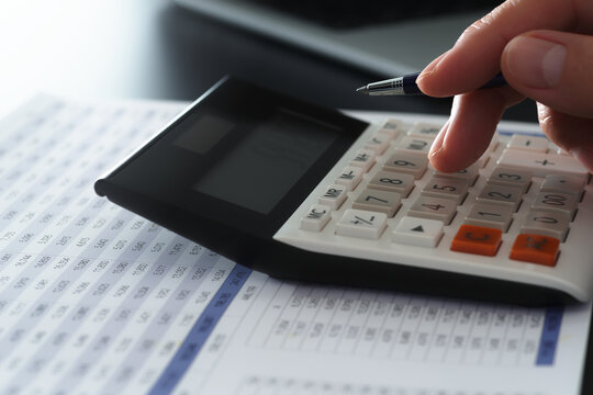 Business financial analysis and calculations. Accounting management and budget planning. Close-up of businessman's hand using calculator on financial report.