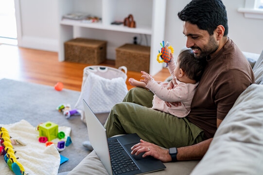 Parent multitasking with baby and laptop on couch