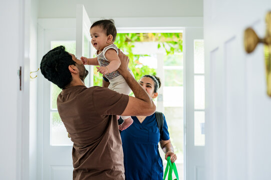 Father holding his baby in a doorway as the mother walks inside with bags