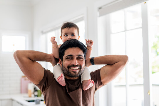 Father carrying child on shoulders inside a home with bright sunlight coming through windows