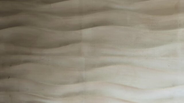 Old wave-shaped plaster wall texture with cracks and damp stains. 4K industrial background featuring weathered grey surface before renovation. Raw atmospheric detail showing 3D relief shadows