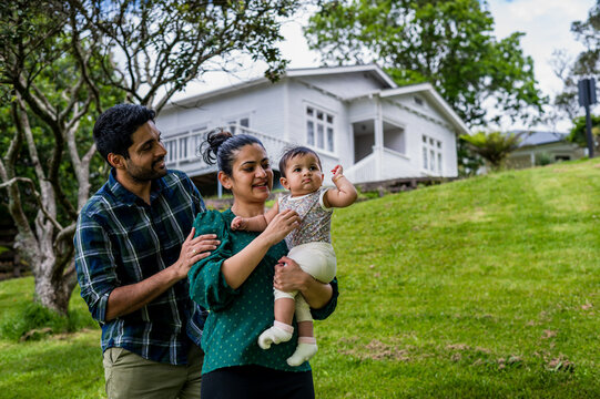 Parents having quality time with their baby while standing on grass by their house