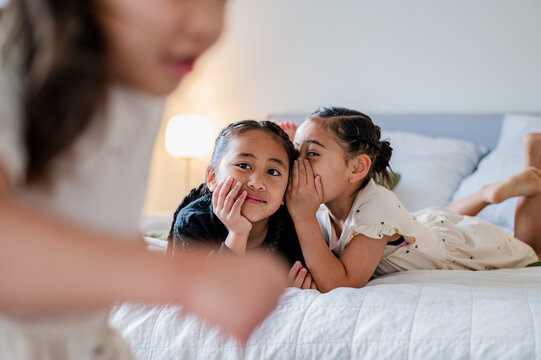 Young girl whispering on brothers ear while lying on their belly on the bed