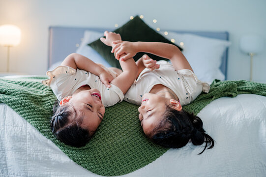 Two sisters laughing and playing on bedroom bed