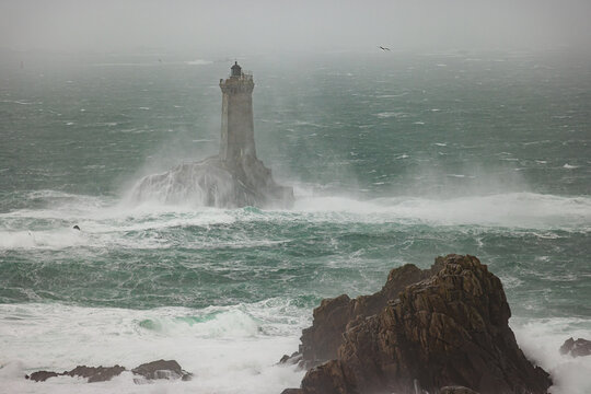 View of the La Vieille lighthouse at Pointe du Raz surrounded by crashing waves and mist in a stormy sea in Plogoff, Brittany, France.
