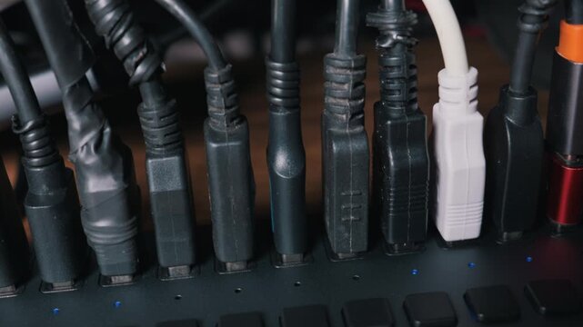 Close-up dolly shot of multiple USB cables plugged into a powered multi-port hub. The device has blue indicator lights and connects various peripherals. Concept of digital connectivity.