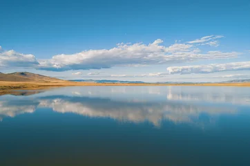 Aerial view of the clouds reflect on still water at the lake during the day in a natural landscape with mountains in the background © Evgenii Bakhchev