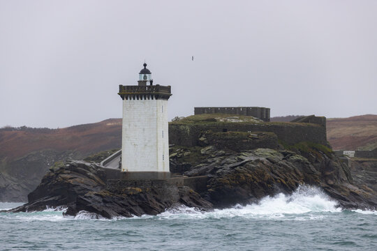 View of Kermorvan Lighthouse on a rocky islet with crashing waves and a stone fort under an overcast sky Le Conquet, Bretagne, France.