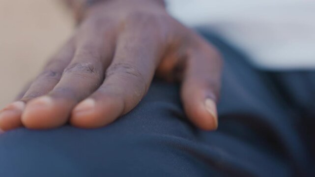 Black runner palm on thigh closeup, black male sprinter steadying hand on dark training shorts with dusty fingertips tense outdoor moment of concentration before sprint, breath control and resolve