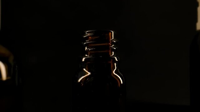 A pills falls into an amber pharmacy bottle standing on black background under subdued lighting. Concept of pharmacy, healthcare, medication, treatment, medical packaging and pharmaceutical
