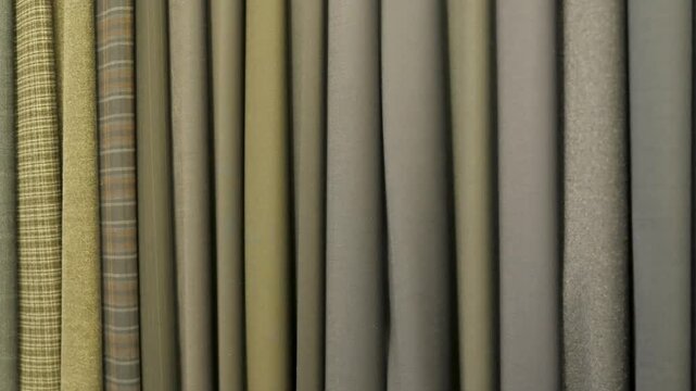 diverse selection premium wool textile rolls featuring various shades olive green khaki grey patterns including herringbone tweed check designs hanging neatly workshop display