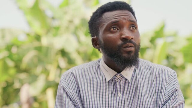 Black man looking upward among palms, patterned shirt and beard framed by bright foliage candid reaction sequence with expressive eyes suggesting vendor, preacher, or market storyteller taking