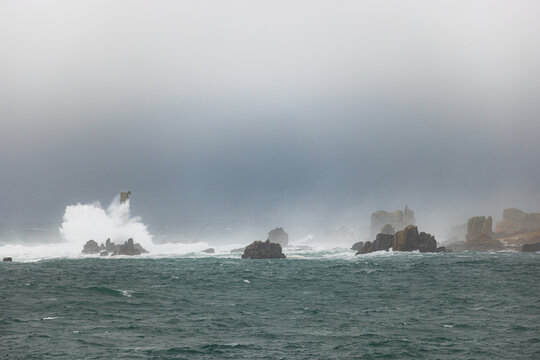 View of powerful waves crashing against jagged rocks in a misty and stormy sea Ushant, Brittany, France.