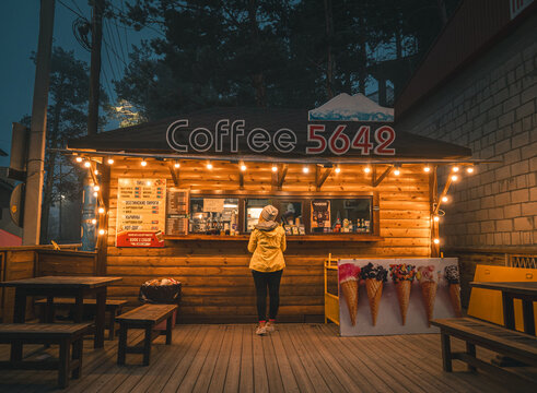 Azau, Russia - July 25,2021: Woman waits at the illuminated coffee stand in a forested area during the evening