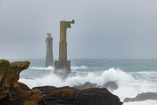 View of the Nividic lighthouse and its concrete pylon surrounded by crashing waves and rough sea under an overcast sky in Ushant, Brittany, France.