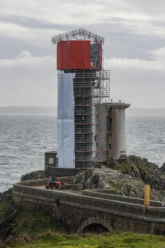 View of Le Petit Minou lighthouse under renovation with scaffolding and workers on a rocky cliffside overlooking the sea in Plouzane, Bretagne, France.