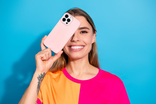 Young woman with pink phone against blue background smiling in bright casual fashion portrait