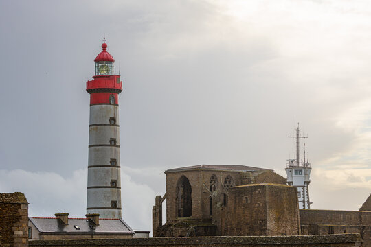 View of the Pointe Saint-Mathieu lighthouse and abbey ruins under a cloudy sky in Plougonvelin, Brittany, France.