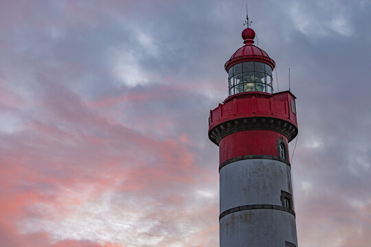 View of the Pointe Saint-Mathieu lighthouse with its red lantern room under a pink sunset sky in Plougonvelin, Brittany, France.