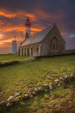 View of the historic Saint-Mathieu lighthouse and chapel ruins under a dramatic sunset sky at Pointe Saint-Mathieu, Plougonvelin, Brittany, France.
