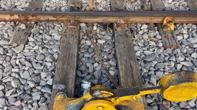 Railroad switch mechanism is revealed in detail as the camera slowly pulls back and tilts up over rails, ballast and wooden sleepers.