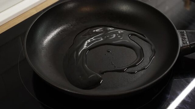 Empty nonstick frying pan with small amount of oil heating on home stovetop.