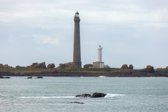 View of the Ile Vierge lighthouse and its smaller predecessor standing on a rocky island under a cloudy sky in Plouguerneau, Bretagne, France.