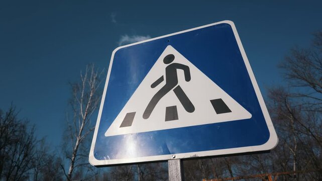 Blue pedestrian crossing traffic sign stands against a bright sky and bare trees. The safety concept highlights traffic regulations and pedestrian rights for careful urban street navigation.