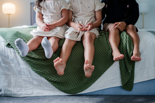 Three young kids sitting closely with small legs dangling freely on the bed
