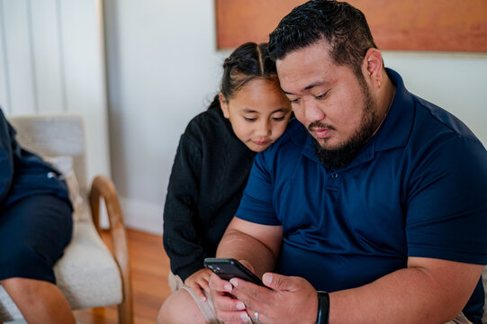 Samoan man scrolling through his phone while son looks over his shoulder