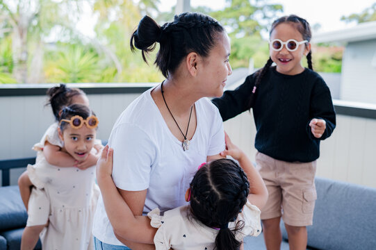 Teenage girl bending forward to pickup and carry younger sister in the balcony while playing