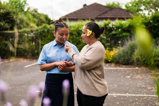 Niuean mum letting teenage daughter smell a flower while holding hands in an open parking space