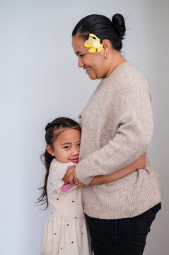Young girl hugging mum with yellow flower on her ear inside home