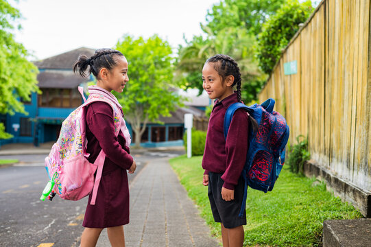 Two young school kids carrying backpacks standing on the sidewalk facing each other