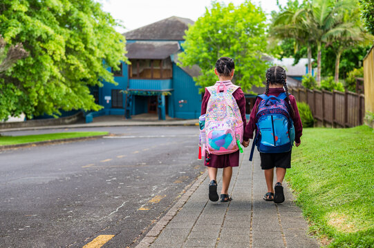 Two young kids in school uniform walking on the sidewalk holding hands