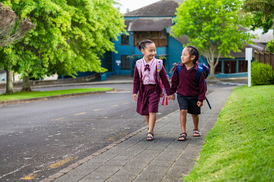 Two young kids in school uniform walking on the sidewalk holding hands