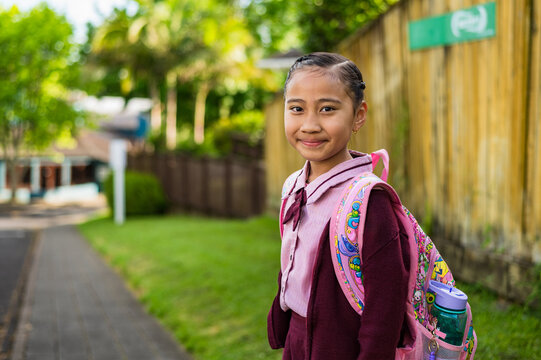 A young girl with a backpack stands on a footpath outside school