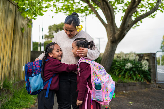 Niuean mum hugging school children wearing backpacks outdoors