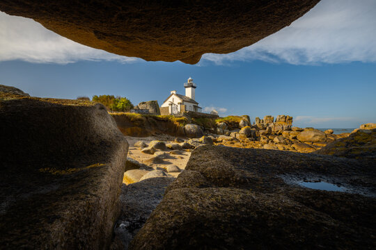 View of Phare de Pontusval lighthouse framed by massive granite boulders on the rocky coast of Plouneour-Brignogan-Plages, Bretagne, France.