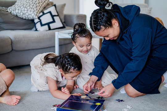 Teenage girl playing with jigsaw puzzles with younger siblings on carpeted floor in the living room