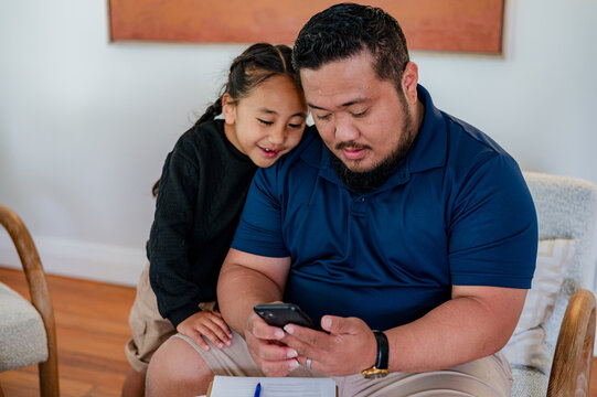 Maori man scrolling through his phone while son looks over his shoulder