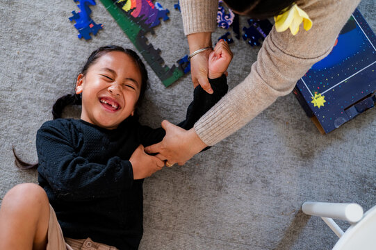 Young Samoan boy lying on the floor surrounded by scattered puzzle pieces tickled by adult hand