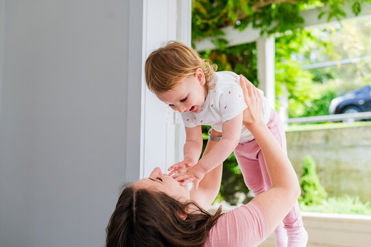 Italian mum sitting in the doorway lifting toddler daughter mid-air playfully