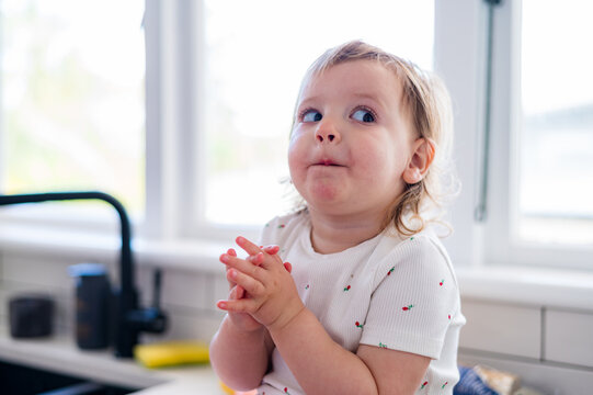 Toddler girl sitting on kitchen counter doing a side eye with hands clasped together